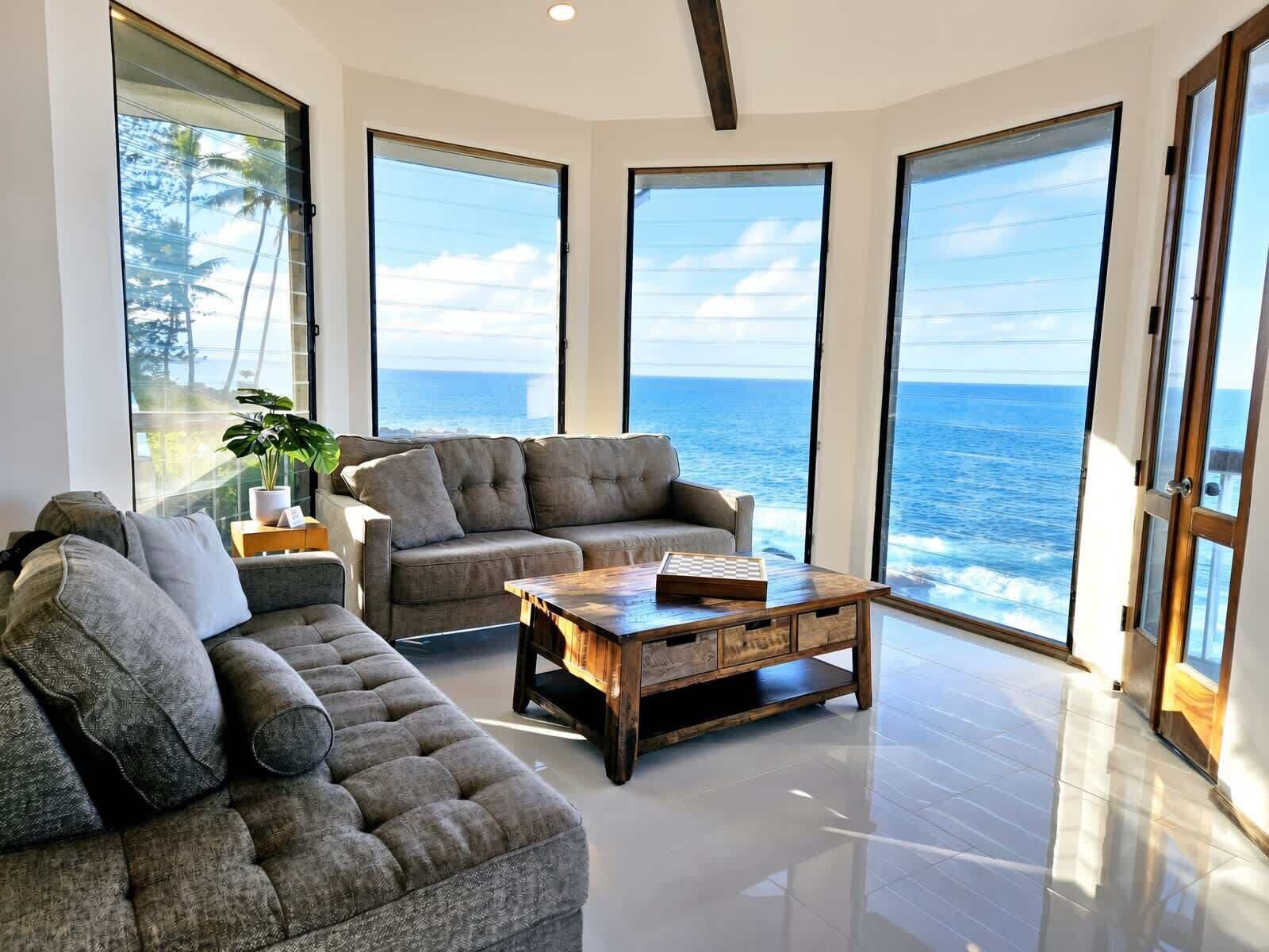 A modern living room with a large window overlooking the sea, a plush sofa, and a wooden coffee table.