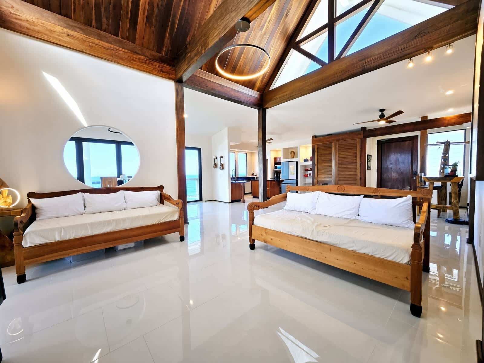 A spacious room with two wooden beds, a large mirror, and a view of the sea.