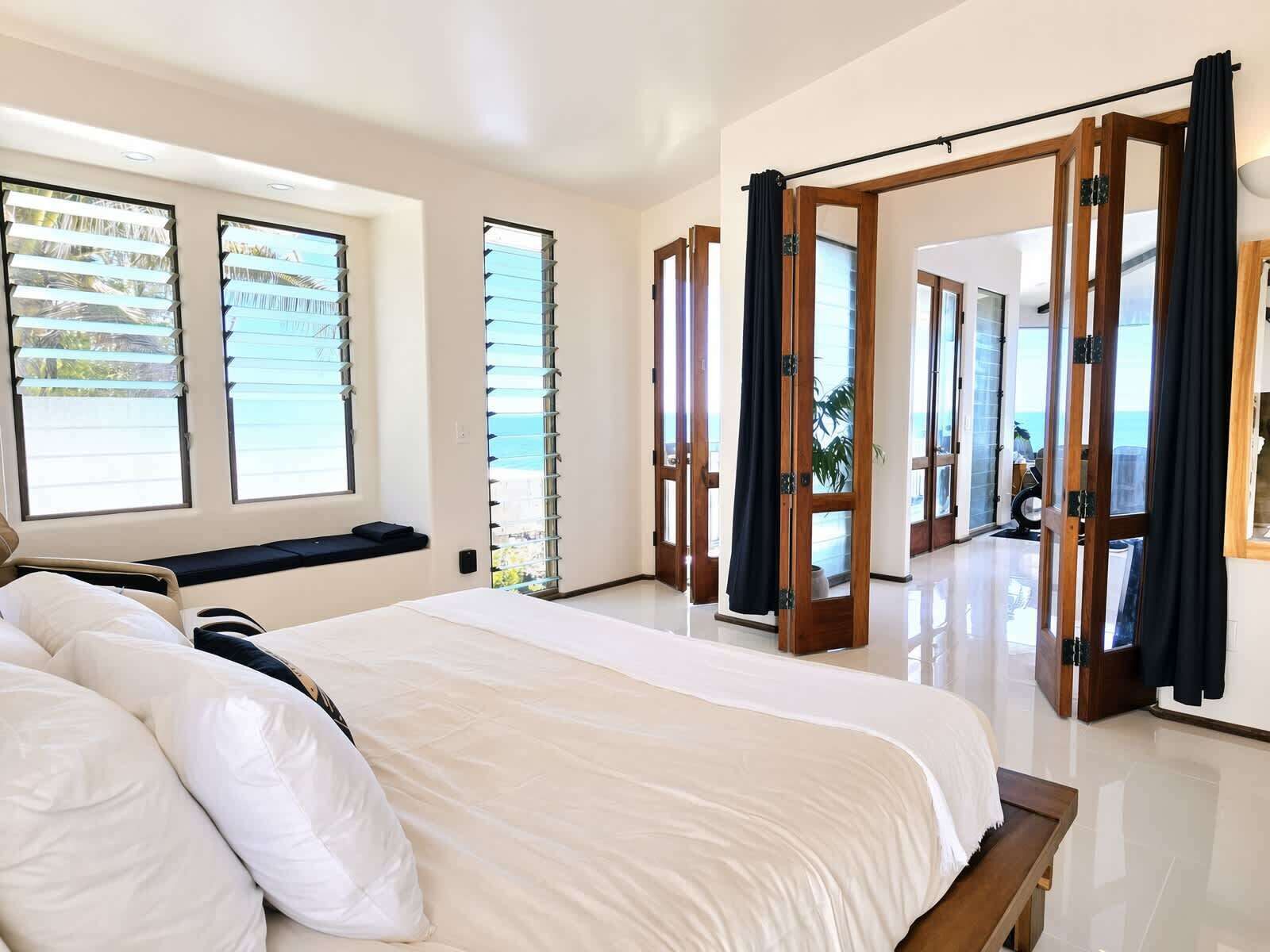 A hotel room with a large bed, a window with blinds, a door with a curtain, and a view of the sea.
