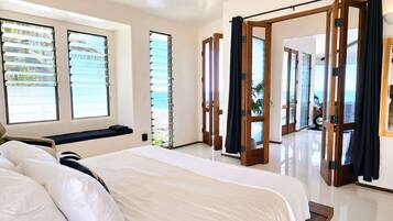 A hotel room with a large bed, a window with blinds, a door with a curtain, and a view of the sea.