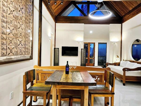 A dining area with a wooden table and benches, a bottle of wine, and a TV mounted on the wall.