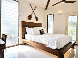 Ein Schlafzimmer mit einem hölzernen Bett, weißer Bettwäsche, einem Deckenventilator und Blick ins Freie.