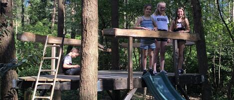 A wooden platform with a slide, surrounded by trees.