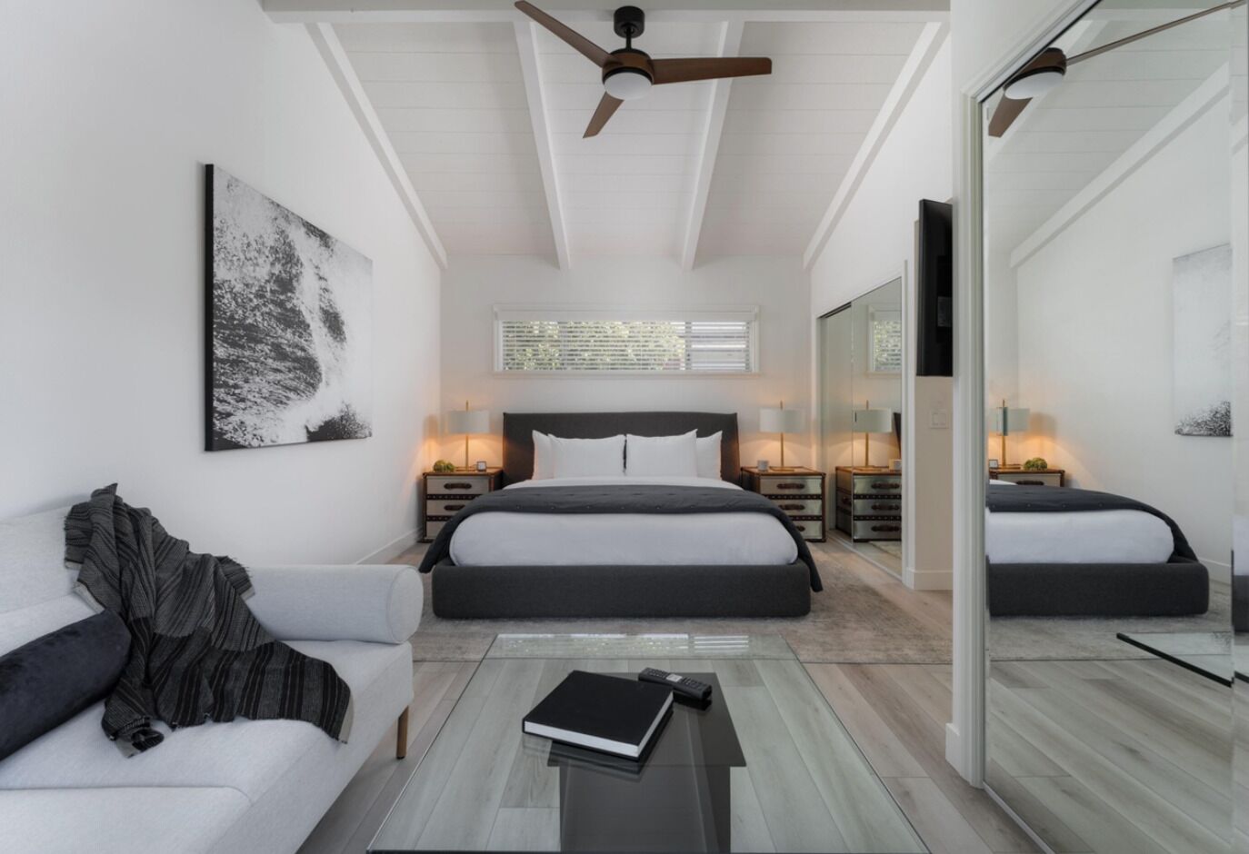 A modern bedroom with a large bed, a sofa, a coffee table, and a ceiling fan.