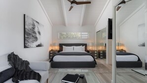 A modern bedroom with a large bed, a sofa, a coffee table, and a ceiling fan.