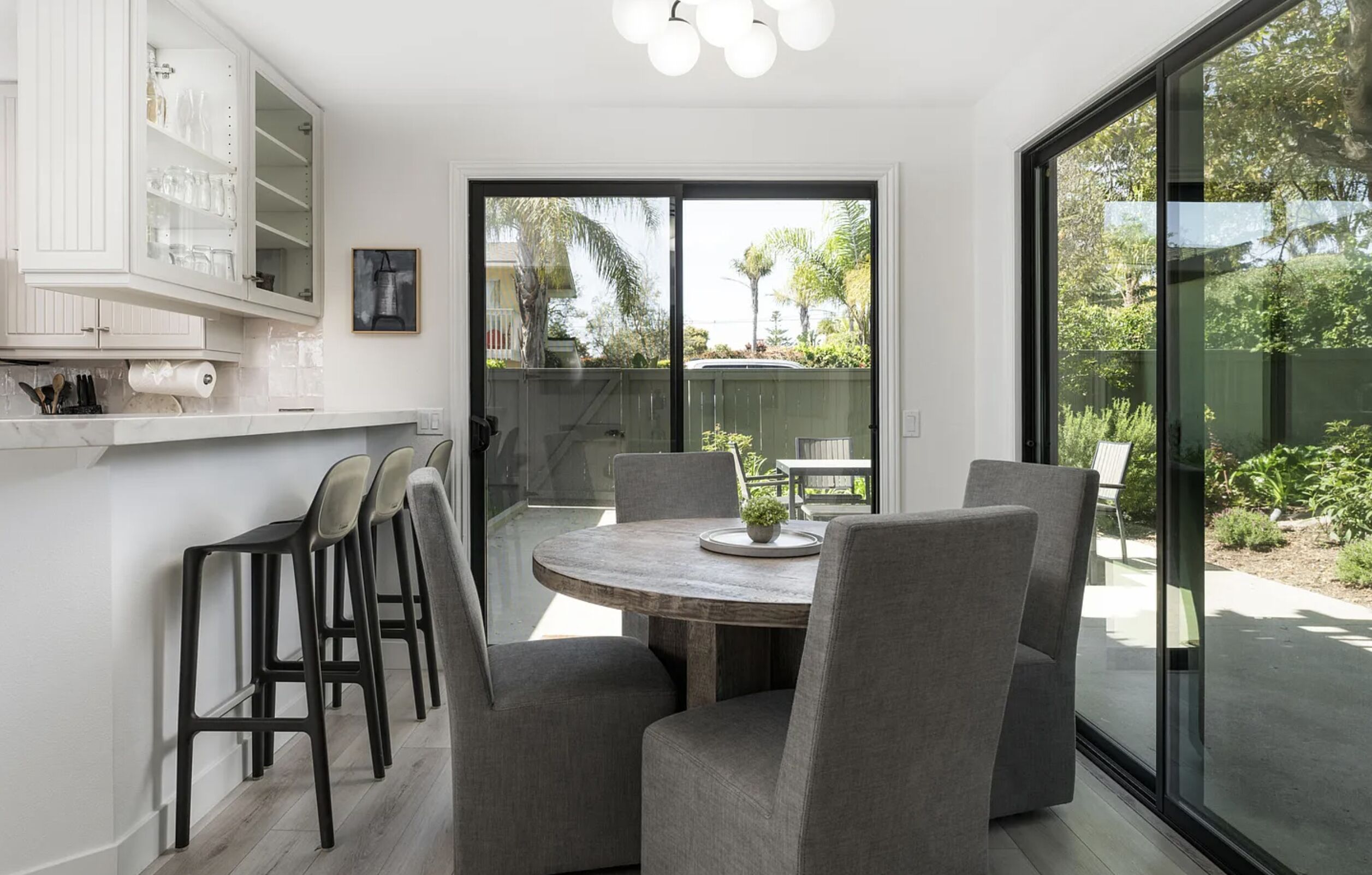 A modern kitchen with a dining area, large windows, and a view of the outdoors.