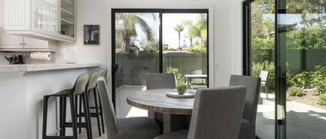A modern kitchen with a dining area, large windows, and a view of the outdoors.