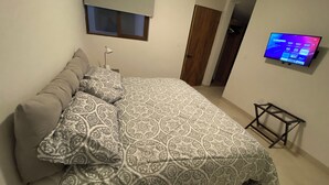 Una camera da letto con un letto, una TV montata a parete e una porta che dà su un'altra stanza.