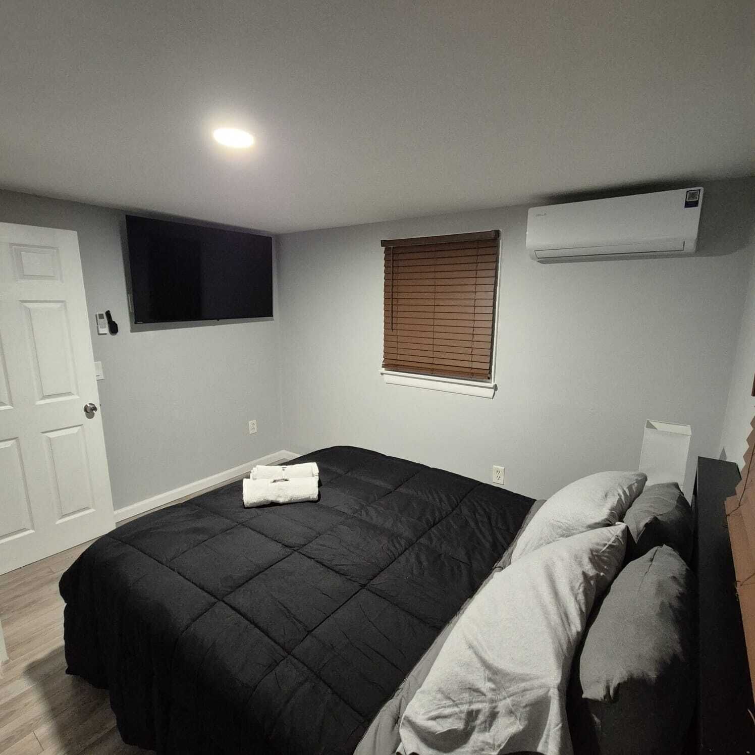 Un dormitorio con cama, ventana con persianas, equipo de aire acondicionado y una puerta.