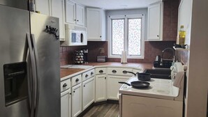 A compact kitchen with white cabinets, a stainless steel refrigerator, a microwave, a stove, and a sink.