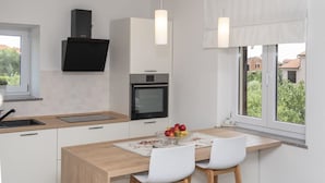 A modern kitchen with a built-in oven, a microwave, and a black range hood. There is a dining table with two chairs and a fruit bowl on the table. - House in Fazana With Private Pool and Beach (Fazana)