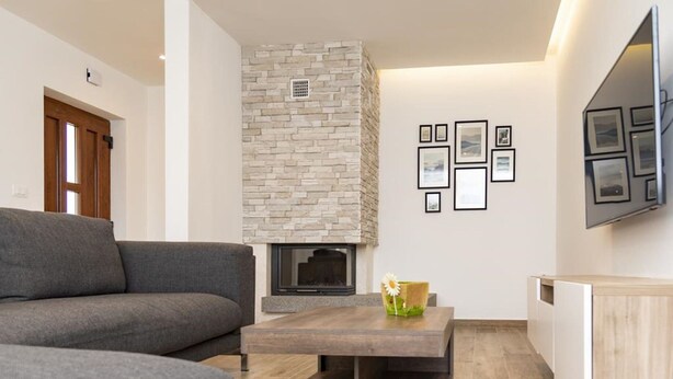 A modern living room with a stone fireplace, a grey sofa, a coffee table with a vase, and a wall-mounted TV. - House in Fazana With Private Pool and Beach (Fazana)