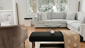 Ein modernes Wohnzimmer mit einem Ecksofa, einem Glastisch, einem schwarzen Hocker und einer Holzbank.