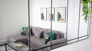 Ein modernes Wohnzimmer mit einem grauen Sofa, einem Glastisch und drei gerahmten Kunstwerken an der Wand.