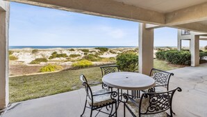Een terras buiten met een ronde tafel en stoelen, met uitzicht op een strand met duinen en groen.