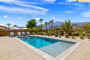 A rectangular swimming pool with a tiled deck, surrounded by lounge chairs and palm trees, with mountains in the background. - Mountain Paradise: Pool & Spa Retreat (La Quinta)