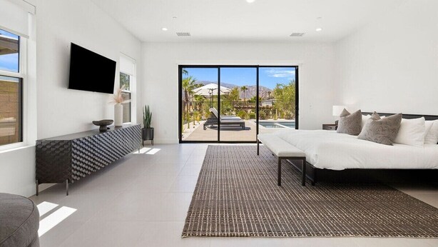 Un dormitorio moderno con cama, televisor, una consola y vistas a una piscina y montañas.
