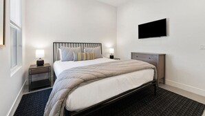 Un dormitorio con cama, mesitas de noche, un televisor de pantalla plana y una ventana.
