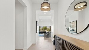 Un pasillo moderno con una consola de madera, un espejo grande y vista a una sala de estar con sofá y ventana.