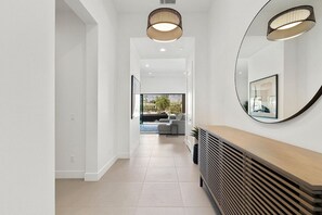 A modern hallway with a wooden console, a large mirror, and a view into a living area with a sofa and a window. - Mountain Paradise: Pool & Spa Retreat (La Quinta)