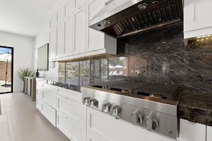 A modern kitchen with a stainless steel range, white cabinetry, and a black marble backsplash. - Mountain Paradise: Pool & Spa Retreat (La Quinta)