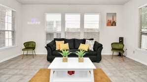 A modern living room with a black sofa, two green chairs, a white coffee table, and a cityscape painting.