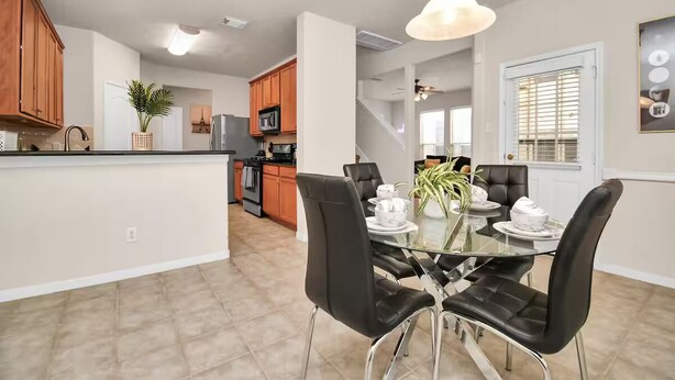 A modern kitchen with wooden cabinets, a central island, and a dining area with a glass table and black chairs.