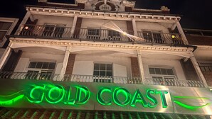 A building with a prominent "GOLD COAST" sign in green neon lights.
