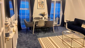 A living room with a dining area, a sofa, a coffee table, and a view of the outside balcony.