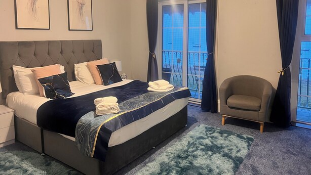 A hotel room with a large bed, a chair, a window with curtains, and artwork on the wall.