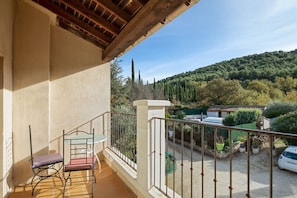 Un balcón con una silla y una mesa, vista a un paisaje verde con árboles y una colina.