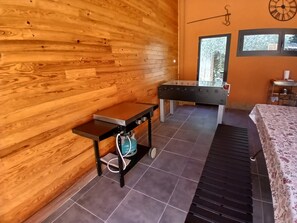 Een kamer met een houten wand, een tafelvoetbaltafel, een bed met een bloemenprint en een raam met uitzicht op bomen.
