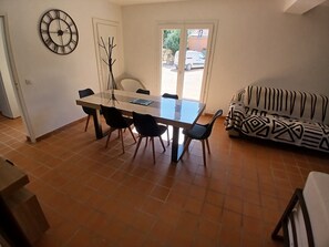 Een eetgedeelte met een glazen tafel, stoelen, een klok aan de muur en een gestreept bankje.