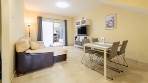 A living room with a sofa, a dining table with chairs, a TV, and a lamp. - Holiday Home 'Vista Hermosa' with Lake View, Wi-Fi and Air Conditioning (Ayamonte)