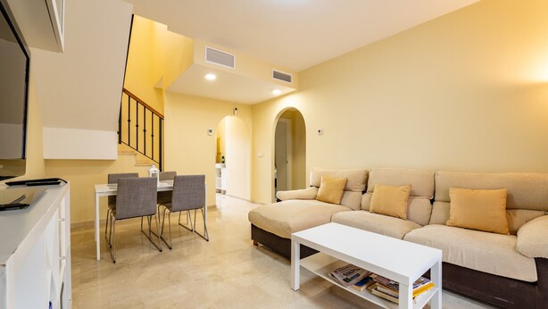 A living room with a sofa, a coffee table, and a dining area with chairs and a table. - Holiday Home 'Vista Hermosa' with Lake View, Wi-Fi and Air Conditioning (Ayamonte)