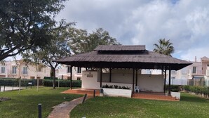 A thatched-roof pavilion with a brick base, surrounded by a well-maintained lawn and a paved path leading to it. - Holiday Home 'Vista Hermosa' with Lake View, Wi-Fi and Air Conditioning (Ayamonte)