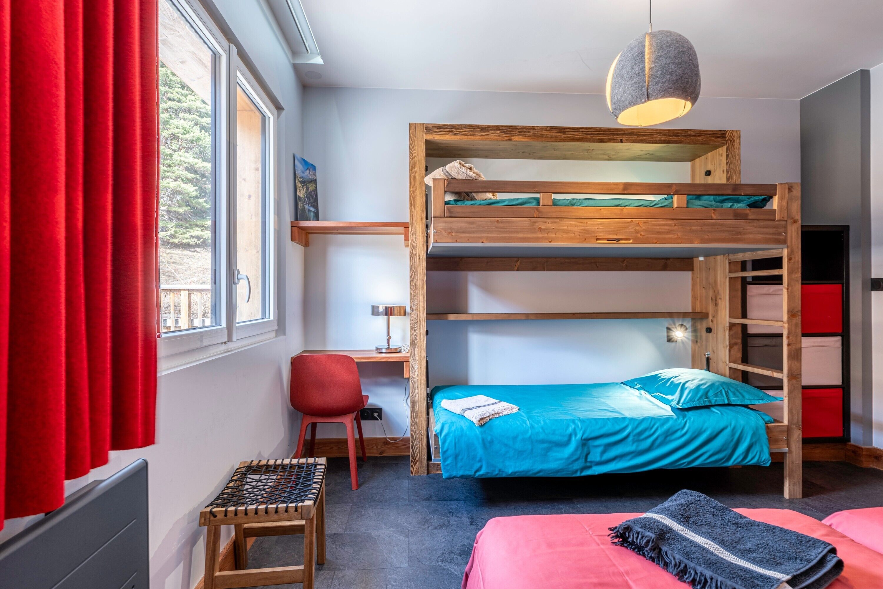 A bunk bed room with a desk, chair, and a hanging light fixture.