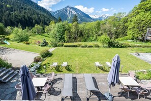 A deck with outdoor seating, a view of a mountainous landscape, and a wooden staircase.