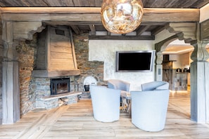 A rustic interior with a stone fireplace, a flat-screen TV mounted on the wall, and modern seating.