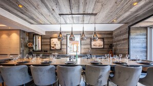 Un espace de restauration moderne avec une longue table, des chaises grises et des luminaires suspendus.