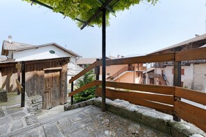 A wooden staircase leading to a building with a stone base, surrounded by other buildings and a tree.