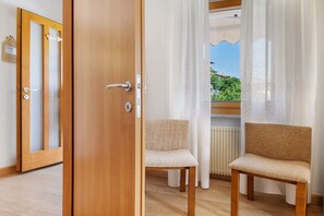 A room with a wooden door, two chairs, a radiator, and a window with curtains.