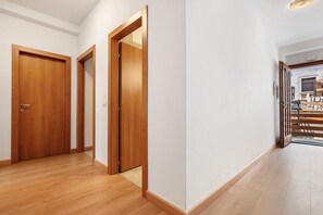 A hallway with wooden doors, a white wall, and a wooden floor.