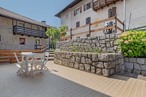 A courtyard with a stone wall, a wooden bench, and a table with chairs.