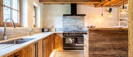A kitchen with wooden cabinetry, a stainless steel sink, a built-in oven, and a stone backsplash.