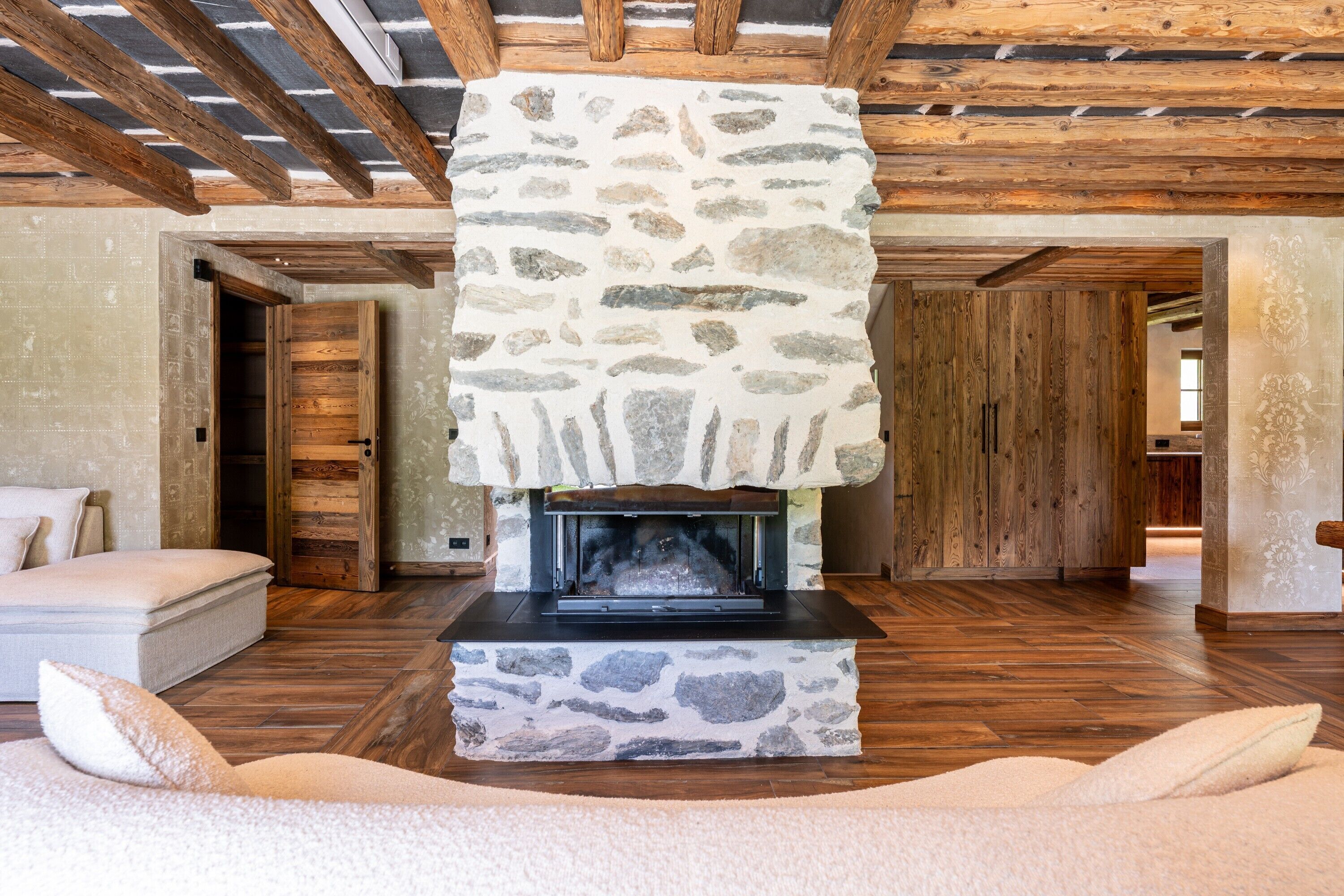 Una chimenea de piedra con repisa de madera, un sofá con cojines y piso de madera.
