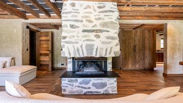 Una chimenea de piedra con repisa de madera, un sofá con cojines y piso de madera.