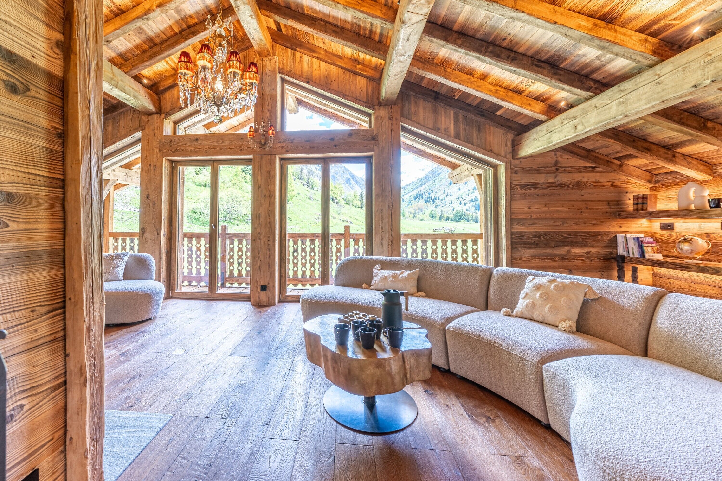 Interior de una cabaña de madera con un sofá grande, una mesita redonda y vistas del exterior a través de amplias ventanas.