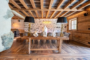Un interior rústico de madera con una pared de piedra, vigas de madera, una mesa central con esculturas de animales y un candelabro.