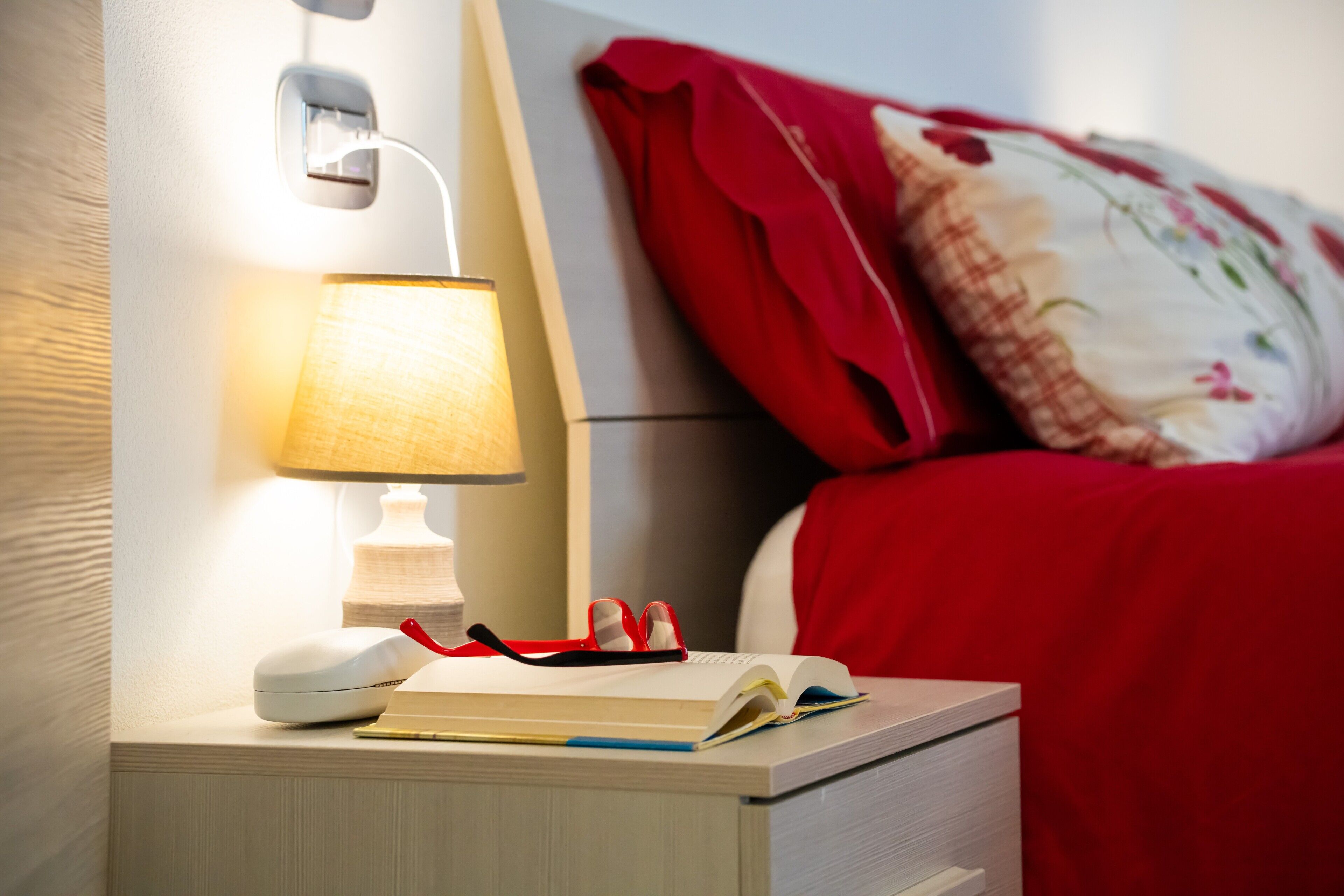 Une table de chevet avec une lampe, un livre et une paire de lunettes.